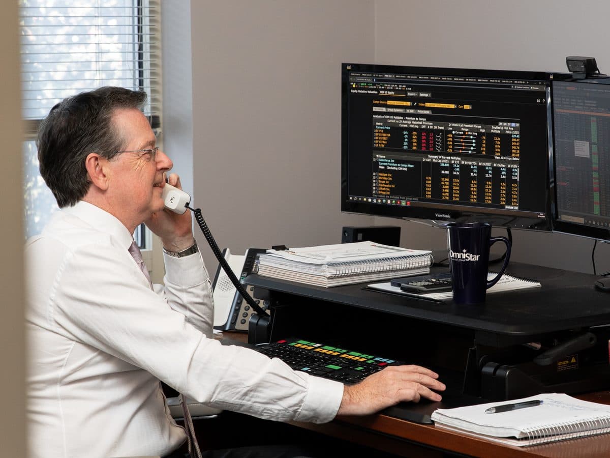 An OmniStar advisor at his desk, on the phone, with market data on the screens in front of him